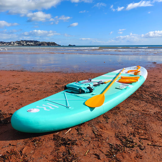Turquoise paddleboard with a yellow paddle on a sandy beach with ocean and sky in the background