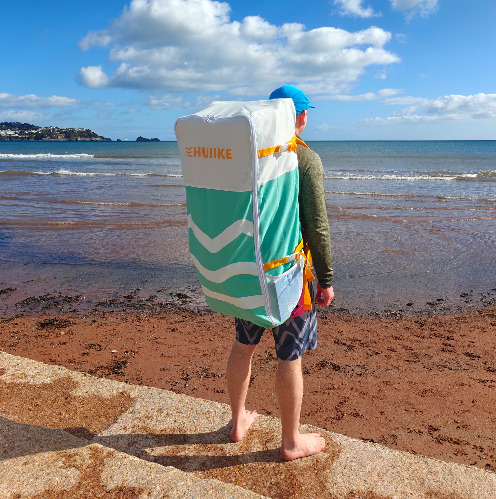 Person with a green and white SUP  backpack on a beach
