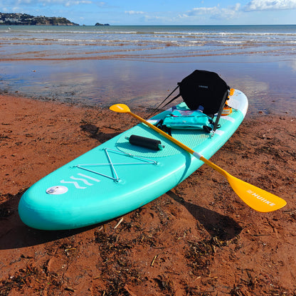 Turquoise paddleboard kayak with a yellow paddle on a sandy beach with ocean in the background